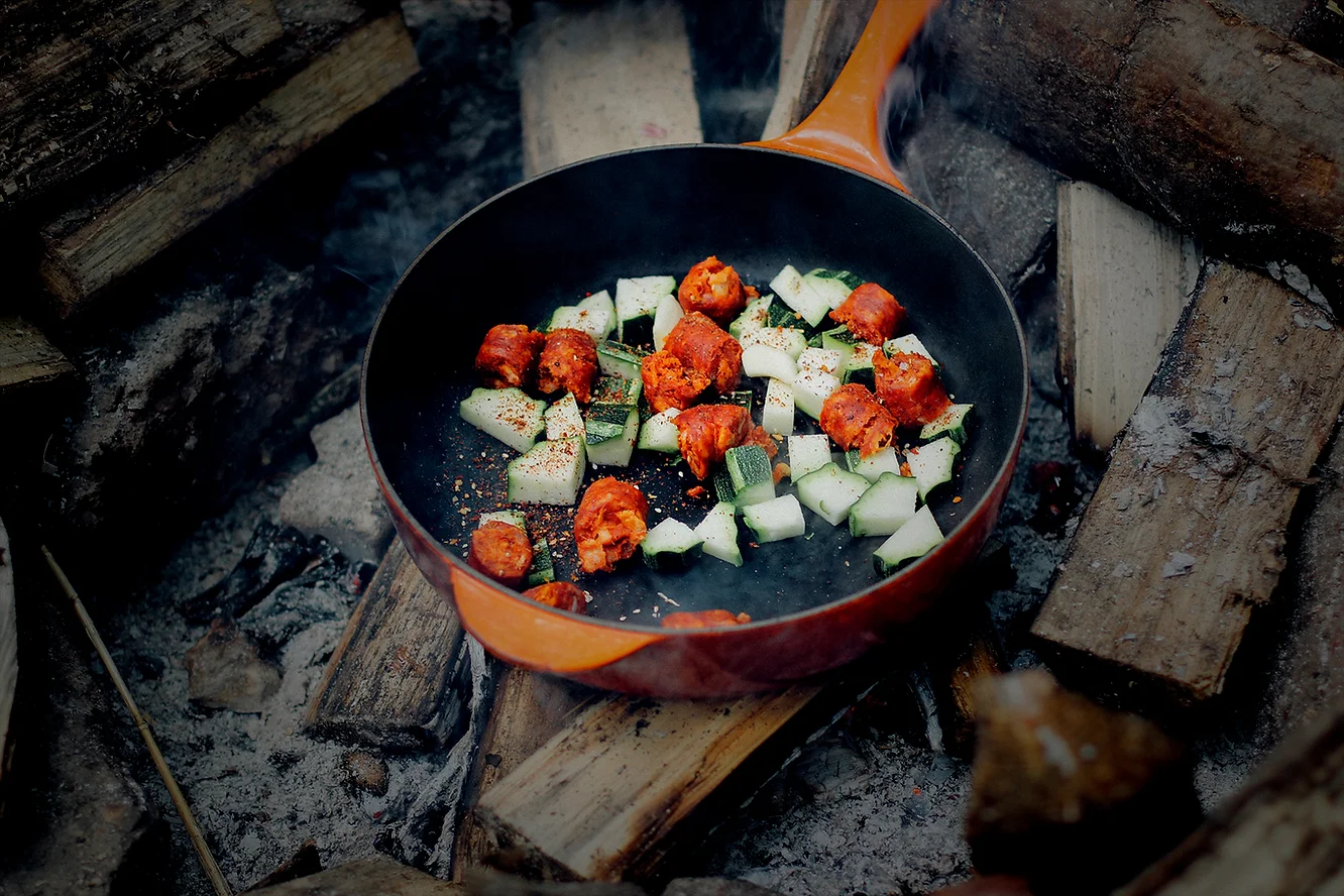 A frying pan filled with grilled veggies on a log fire