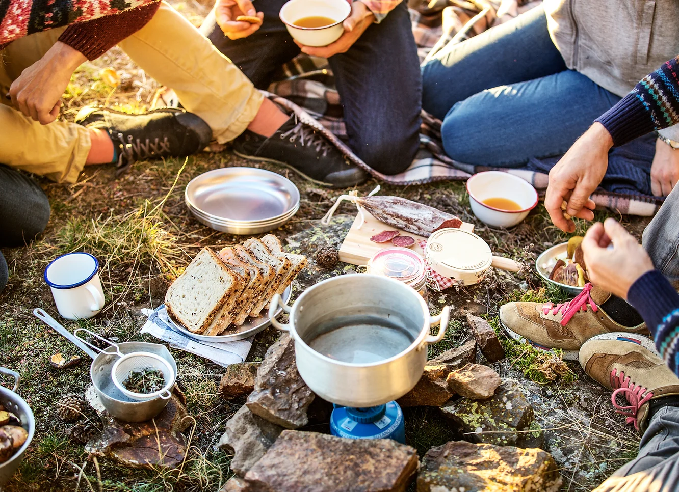 a group of campers enjoying a varied breakfast from a camp stove, including bread and sausage.