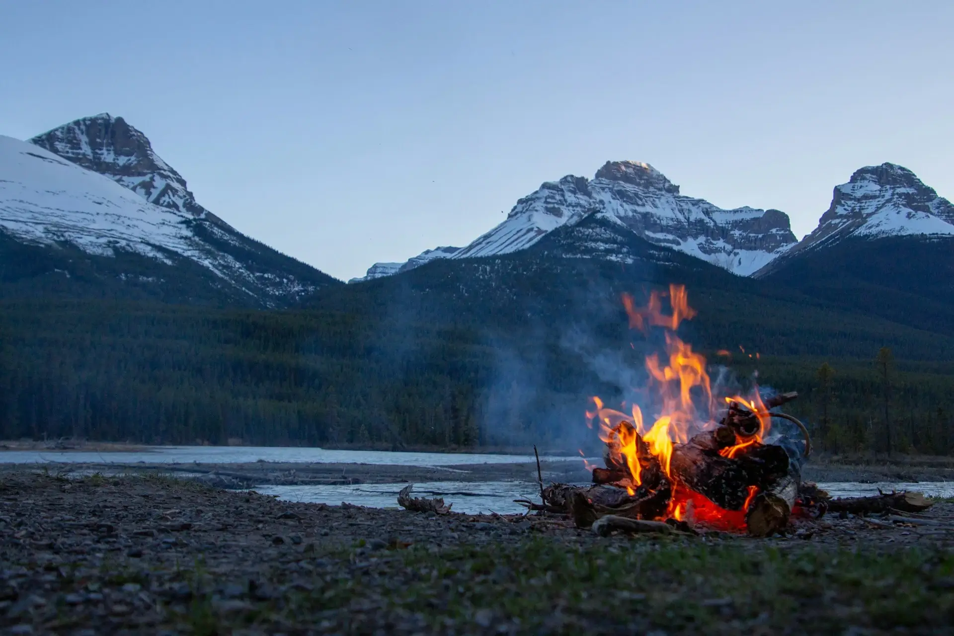 A campfire burning at dusk in front of a glacial mountain backdrop