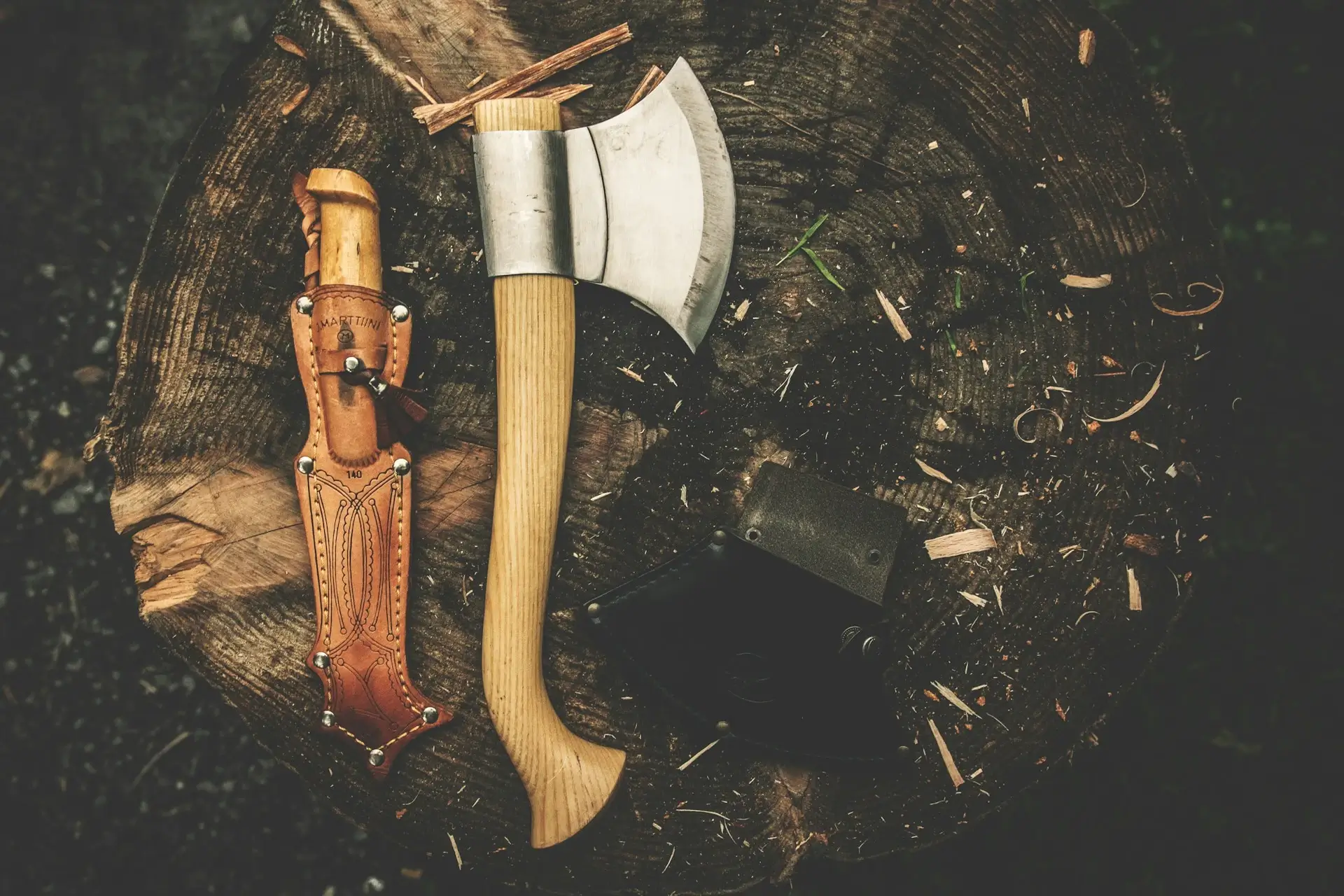 A knife and a hatchet side by side in the dirt outdoors